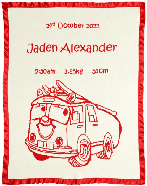 Merino baby blanket with red fire truck design, birth details, and red satin border on natural background.
